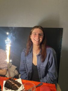 Kiah smiles widely at the camera, and on the red tabletop sits a large slice of chocolate cake with a lit sparkler. 