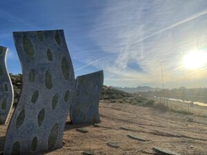 On sand stand stones cut like wavy prisms, blue, with green teardrop shapes. The sun backlights the image. 