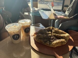 Two iced drinks sit on a desk next to a flatbread covered in seeds. 