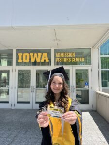 Solenn holding her tour guide name tag outside AVC in graduation regalia.