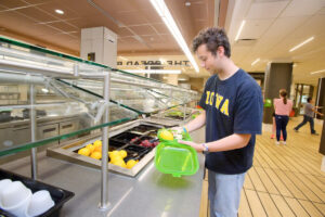 A student picking out food to add to their to go box.
