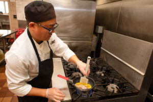 A chef making eggs on a stove.