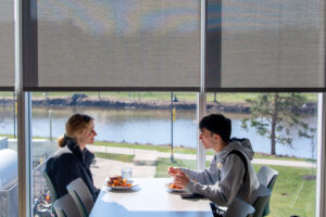 Two people sitting by the window of Catlett dining hall with plates of food, talking to each other.
